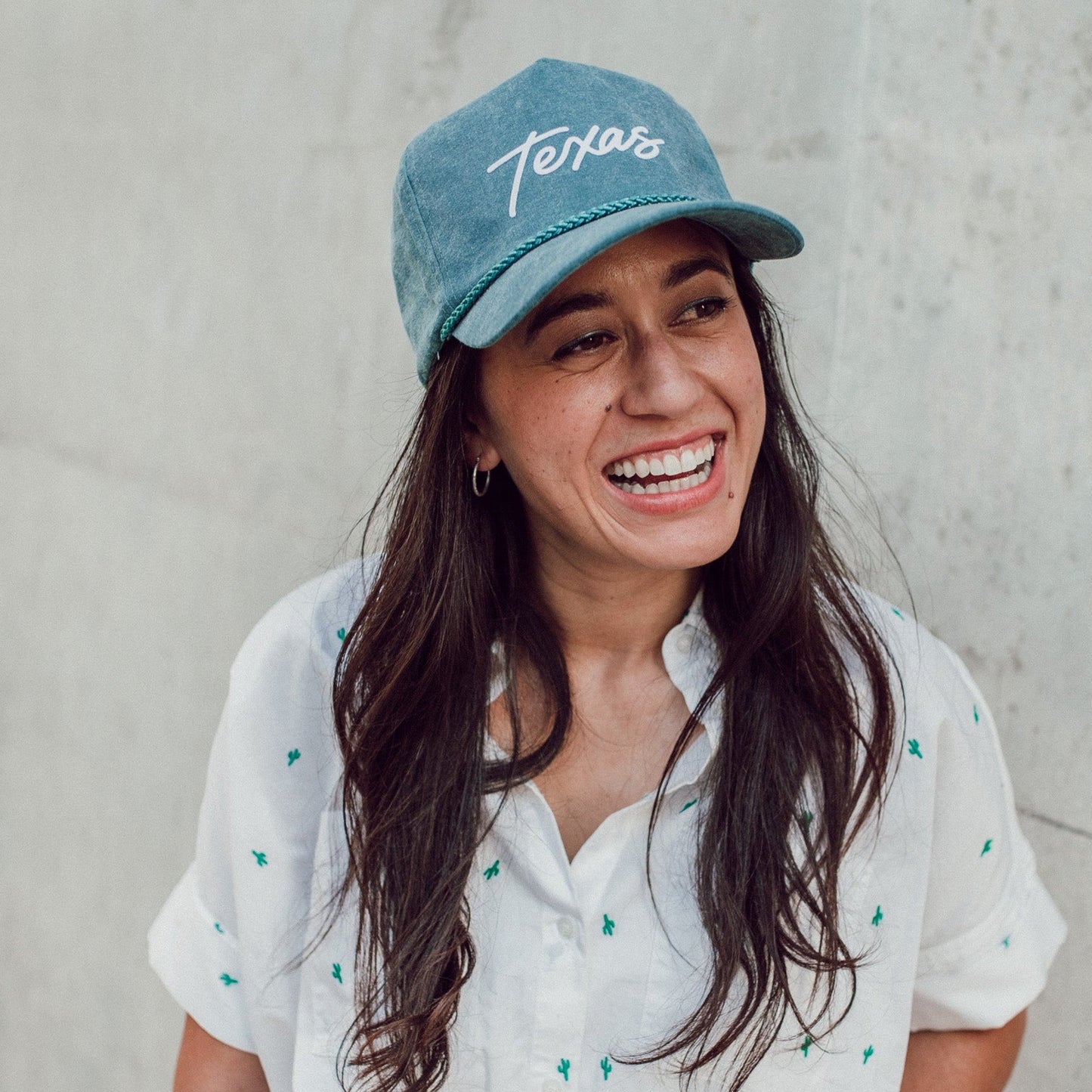 Woman wearing a blue cap with 'Texas' text against a concrete wall