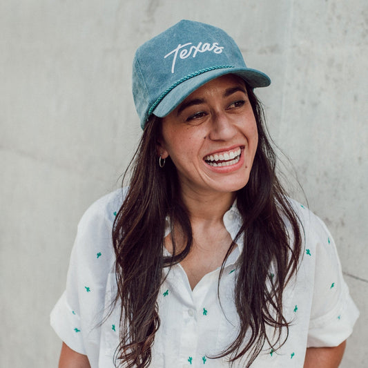 Woman wearing a blue cap with 'Texas' text against a concrete wall